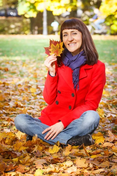 Mulher sorridente no parque de outono com folhas de laranja nas mãos — Fotografia de Stock