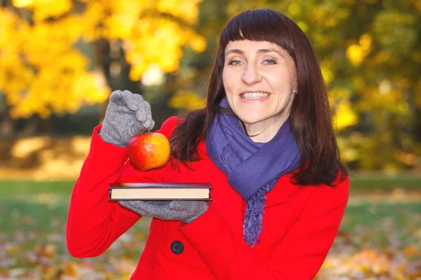 Feliz sorridente mulher segurando livro e maçã no parque de outono — Fotografia de Stock