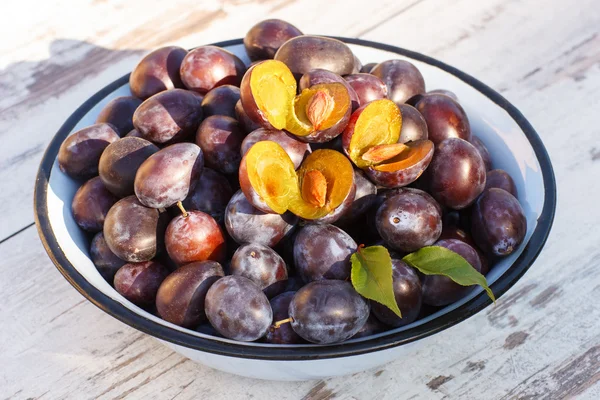 Heap of plums in metal bowl on wooden table in garden on sunny day — Stock Photo, Image