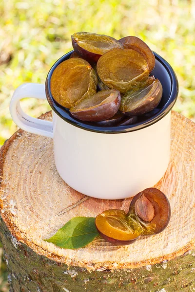 Ameixas em caneca metálica no toco de madeira no jardim no dia ensolarado — Fotografia de Stock