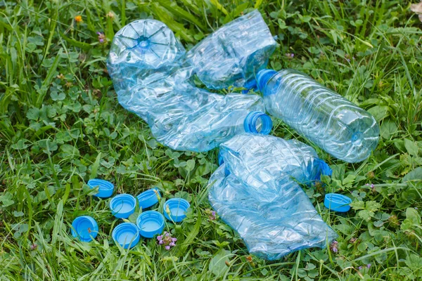 Plastic bottles and bottle caps on grass in park, littering of environment