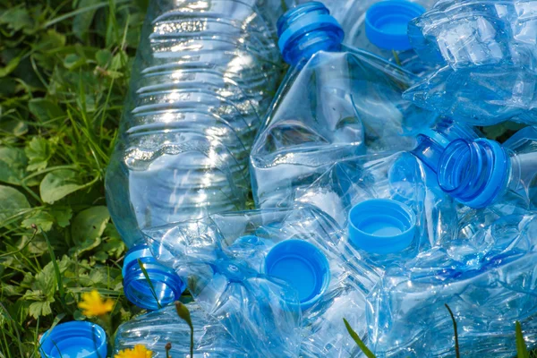 Plastic bottles and bottle caps on grass in park, littering of environment — Stock Photo, Image