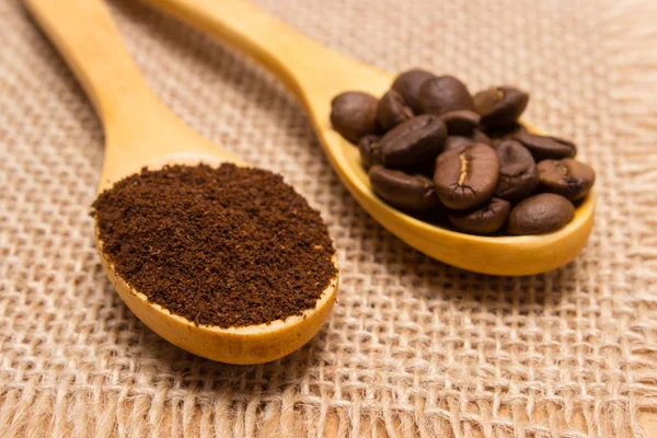 Ground coffee and grains with wooden spoon on jute canvas — Stock Photo, Image