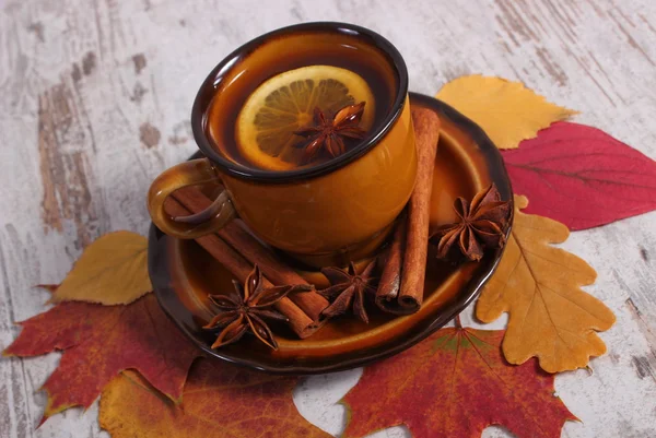 Tasse de thé avec citron, épices et feuilles d'automne sur fond de bois — Photo