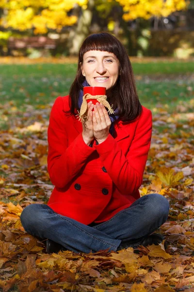 Lachende vrouw in herfst park met warme drank thee of koffie — Stockfoto