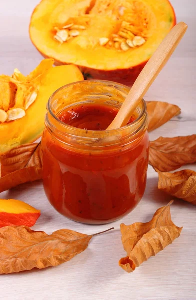 Sauce of pumpkin in glass jar and autumnal leaves on wooden table — Φωτογραφία Αρχείου