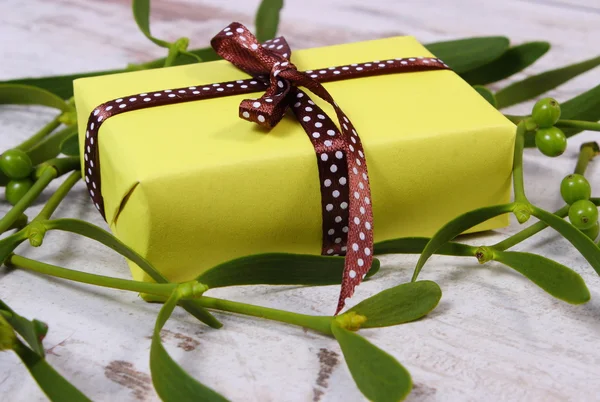 Wrapped gift for Christmas and mistletoe on old wooden background Royalty Free Stock Images