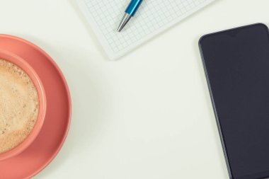 Cep telefonu, not almak için sütlü kahve ve not defteri. Beyaz arka plan. Metin veya yazı için boşluk kopyala