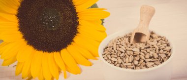 Tahta kepçeli beyaz kasede ay çekirdeği ve güzel sarı çiçek.