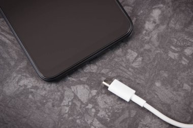 Siyah cep telefonu ve bağlanmamış şarj kablosu. Akıllı telefon şarj oluyor. Siyah arkaplan
