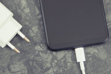 Şarj aletine bağlı siyah akıllı telefon. Telefon şarj ediliyor.