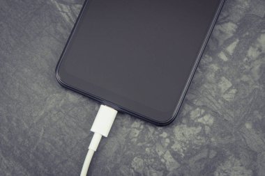 Şarj aletine bağlı siyah akıllı telefon. Telefon şarj ediliyor.
