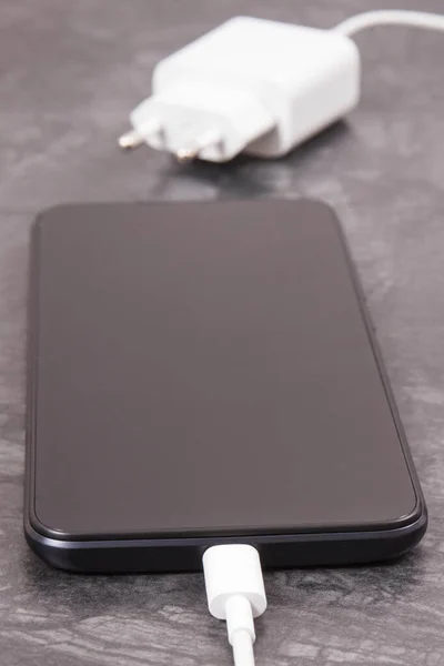 Black smartphone with connected white plug of charger. Telephone charging