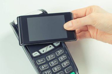 NFC teknolojisiyle ödeme terminali ve cep telefonu kullanan bir kadın eli. Farklı şeyler için para ödemeden.