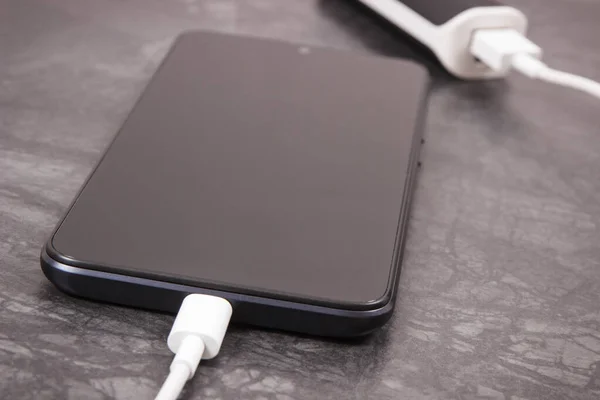 Black smartphone with connected white plug of external powerbank. Mobile phone charging