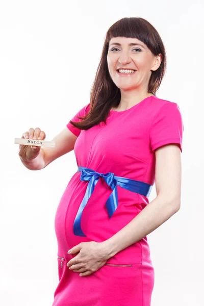 青いリボンでピンクのドレスを着て妊娠中の幸せな笑顔の女性と木製のキューブに書かれた単語行進を示しています 新生児や家族の拡大への期待 — ストック写真