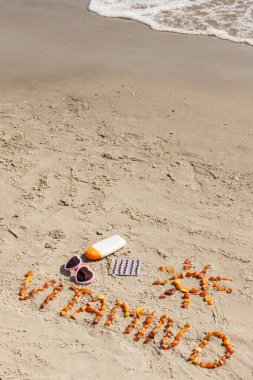 Tıbbi haplar, kehribar taşı ve güneş banyosu için aksesuarlardan yapılmış D vitamini D vitamini, D vitamini eksikliğini önleme konsepti, kumsalda kumdaki kum üzerindeki yazılar için kopyalama alanı