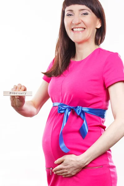 青いリボンとピンクのドレスを着て妊娠中の幸せな笑顔の女性と木製のキューブに書かれた単語2月を示しています 新生児や家族の拡大への期待 — ストック写真
