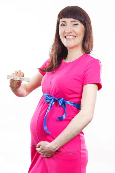 穿着粉色连衣裙的快乐的孕妇 带着蓝色缎带 在木制立方体上写着10月字 对新生儿的期望和家庭的扩大 — 图库照片