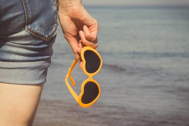 Plajda kalp şeklinde güneş gözlüklü bir kadın eli. Yaz ve tatil zamanı
