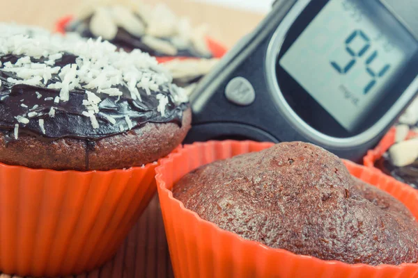 Glucometer with result of measurement sugar level and fresh baked chocolate muffins. Diabetes and dessert for different occasions