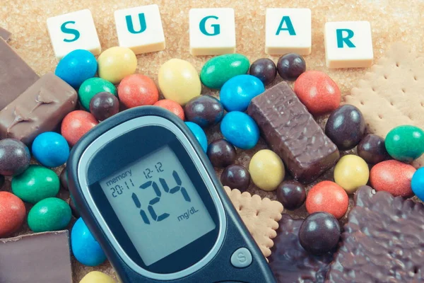 Glucose meter for checking sugar level and heap of sweets containing a lot of sugar. Unhealthy and caloric eating