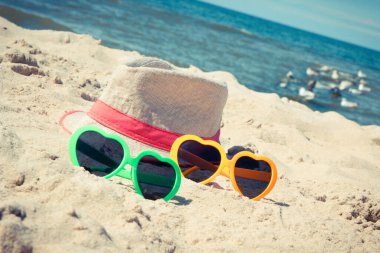 Kumsalda renkli güneş gözlüğü ve hasır şapka. Seyahat ve tatil zamanı kavramı