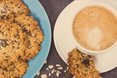 Bir fincan kahve ve ballı taze ev yapımı yulaf ezmesi kurabiyeleri ve farklı sağlıklı tohumlar. Lezzetli çıtır tatlı.