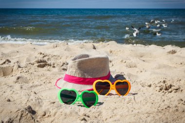 Kumsalda renkli güneş gözlüğü ve hasır şapka. Güneş banyosu sırasında güneş koruması. Seyahat ve tatil zamanı kavramı