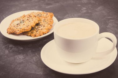 Sütlü bir fincan kahve ve ev yapımı sağlıklı yulaf ezmeli kurabiyeler. Lezzetli çıtır tatlı. Vintage fotoğraf