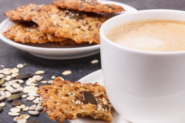 Bir fincan beyaz kahve ve taze ev yapımı yulaf ezmeli kurabiyeler ve farklı sağlıklı tohumlar. Lezzetli çıtır tatlı.