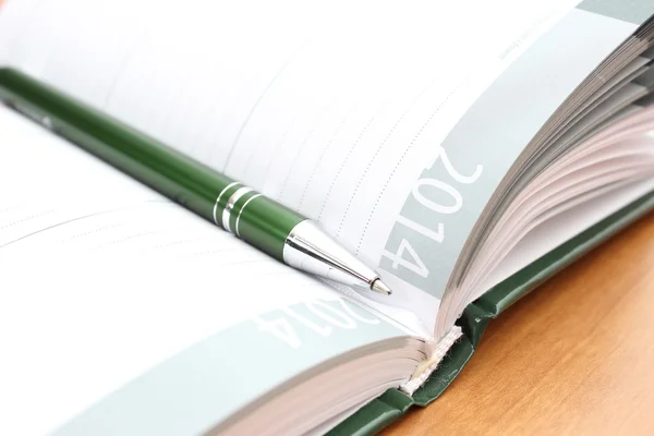 Green pen lying on open organizer on a desk — Stock Photo, Image