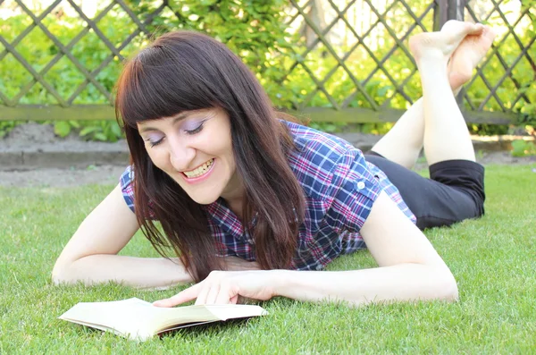 Lächelnde Frau liest Buch auf dem Rasen im Garten — Stockfoto