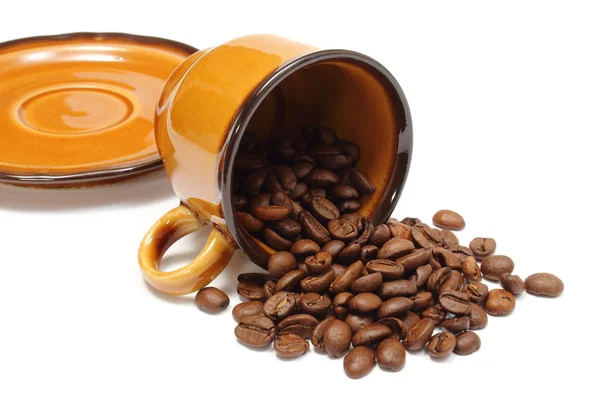 Gekanteld cup en hoop van koffie korrels op witte achtergrond — Stockfoto