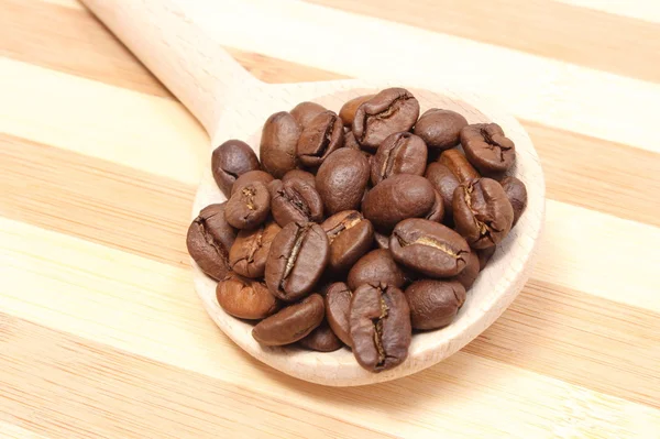 Heap of coffee on wooden spoon. Wooden background — Stock Photo, Image