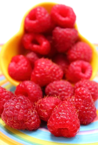 Fresh raspberries pouring out of yellow bowl — Stock Photo, Image