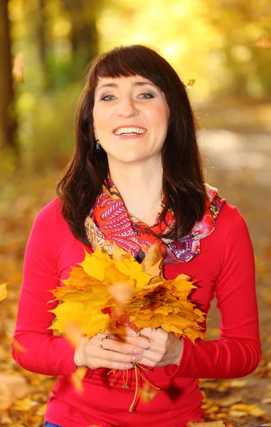 Smiling woman in autumn park with leaves in hands — Stock Photo, Image