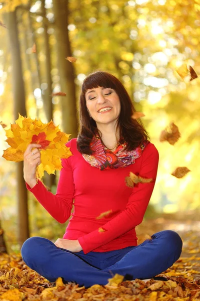 Mujer sonriente en el parque de otoño con hojas en las manos — Foto de Stock