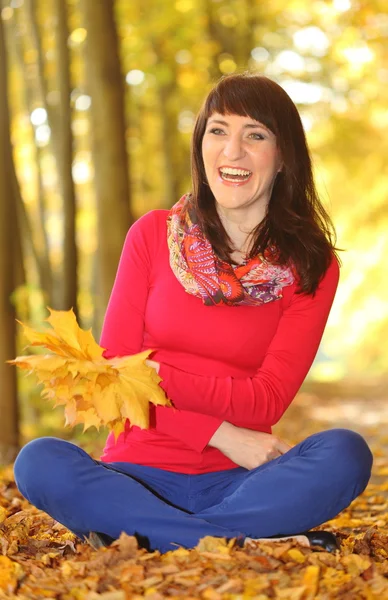 Smiling woman in autumn park with leaves in hands — Stock Photo, Image