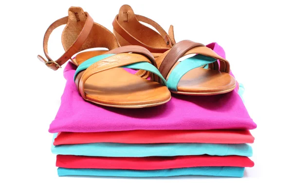 Woman sandals on pile of colorful clothes. White background — Stock Photo, Image