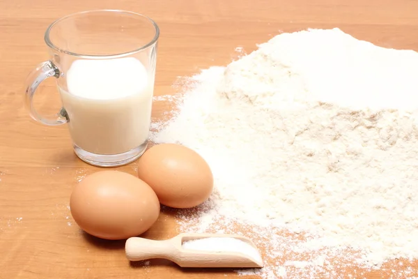 Harina de trigo, vaso de leche y dos huevos en la mesa —  Fotos de Stock