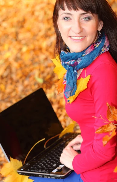 Mujer sonriente con portátil en el parque de otoño —  Fotos de Stock