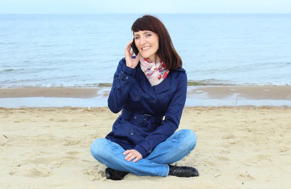 Mujer con teléfono móvil sentada en la playa — Foto de Stock