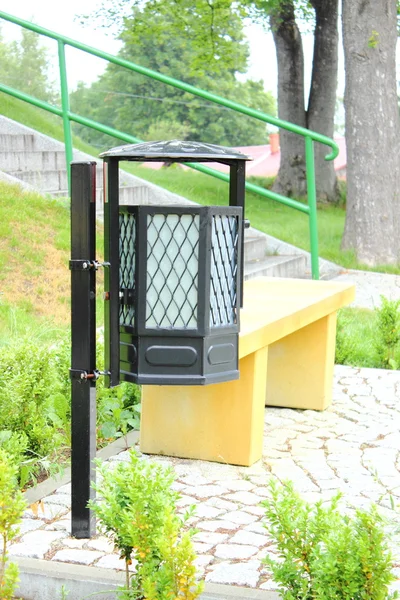 Черная корзина для мусора и желтая скамейка в парке — стоковое фото