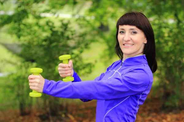 Brunett under fitness tränar med hantlar i höst park — Stockfoto