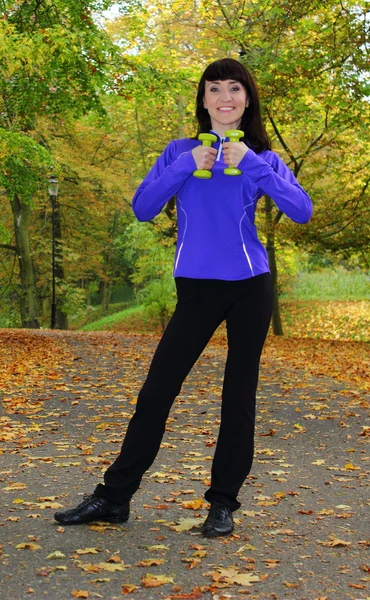 Brunette during fitness exercise with dumbbells in autumn park — Stock Photo, Image
