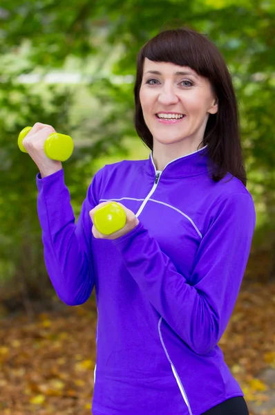 Brunett under fitness tränar med hantlar i höst park — Stockfoto