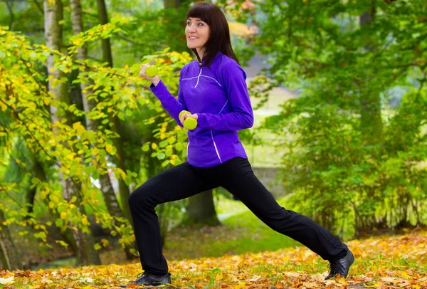 Bruneta în timpul exercițiilor fizice cu gantere în parcul de toamnă — Fotografie, imagine de stoc