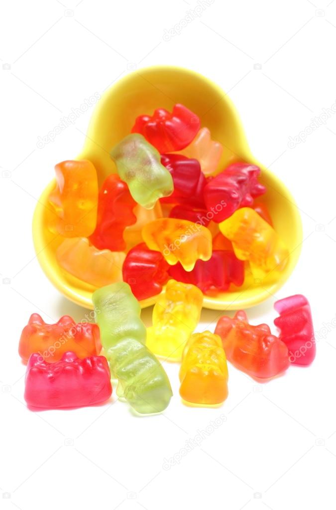 Colorful haribo bear candies pouring out of yellow bowl. White background