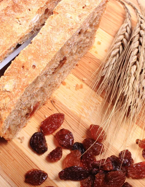 Slicing fresh bread, ears of wheat and raisins — Stock Photo, Image